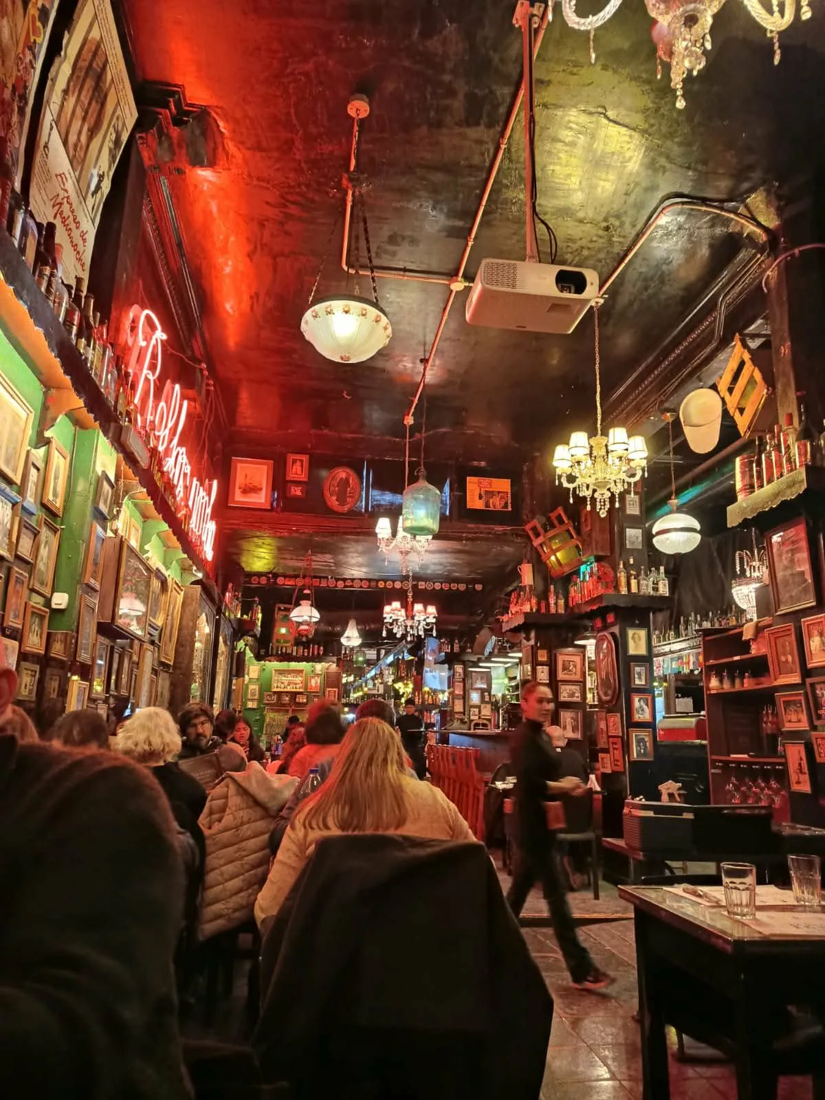 壁一面の額装写真とシャンデリアに囲まれた、夜のバールの店内