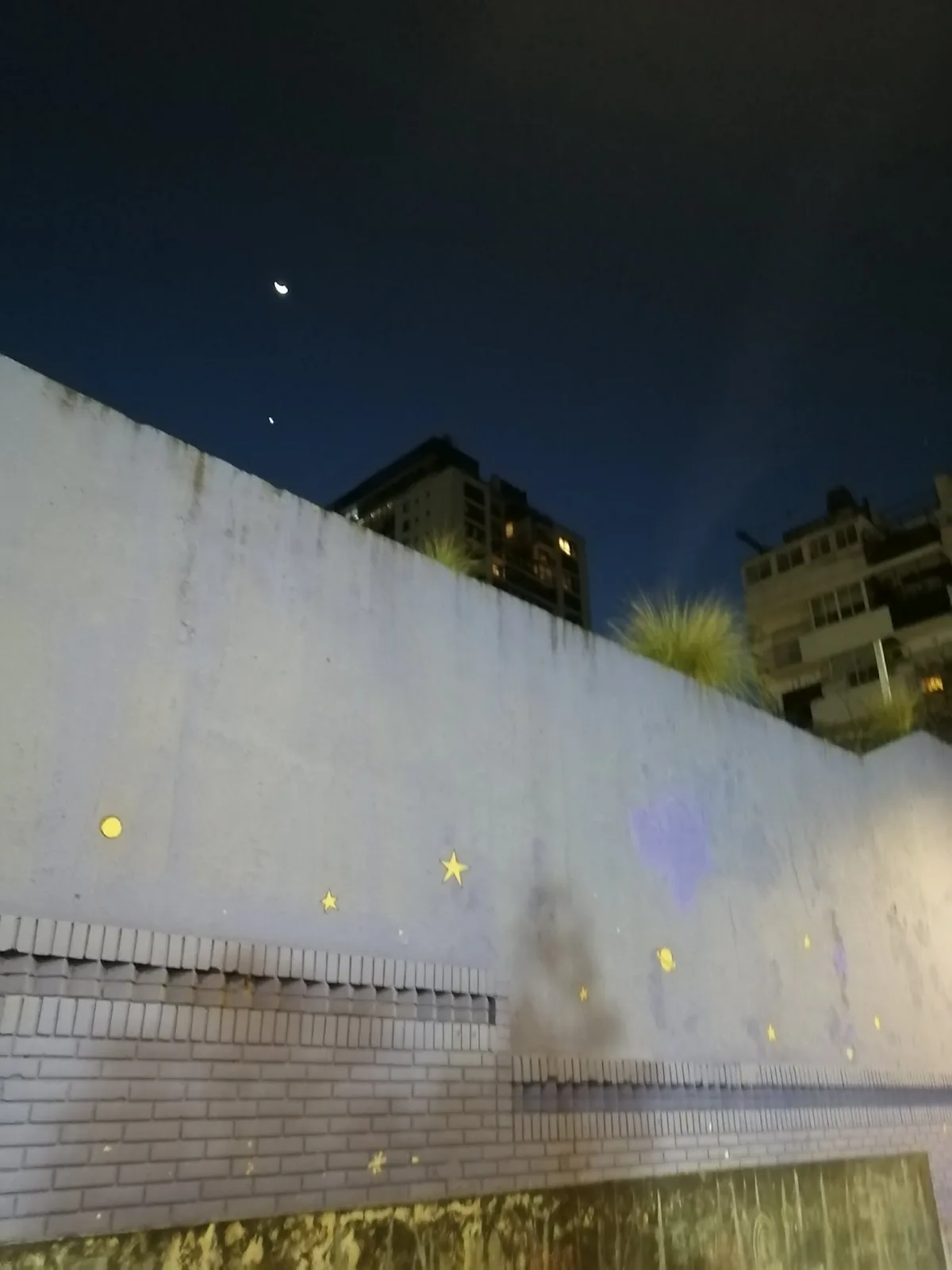 公園の壁に描かれた黄色い星と丸。その上の夜空に細い月が出ている