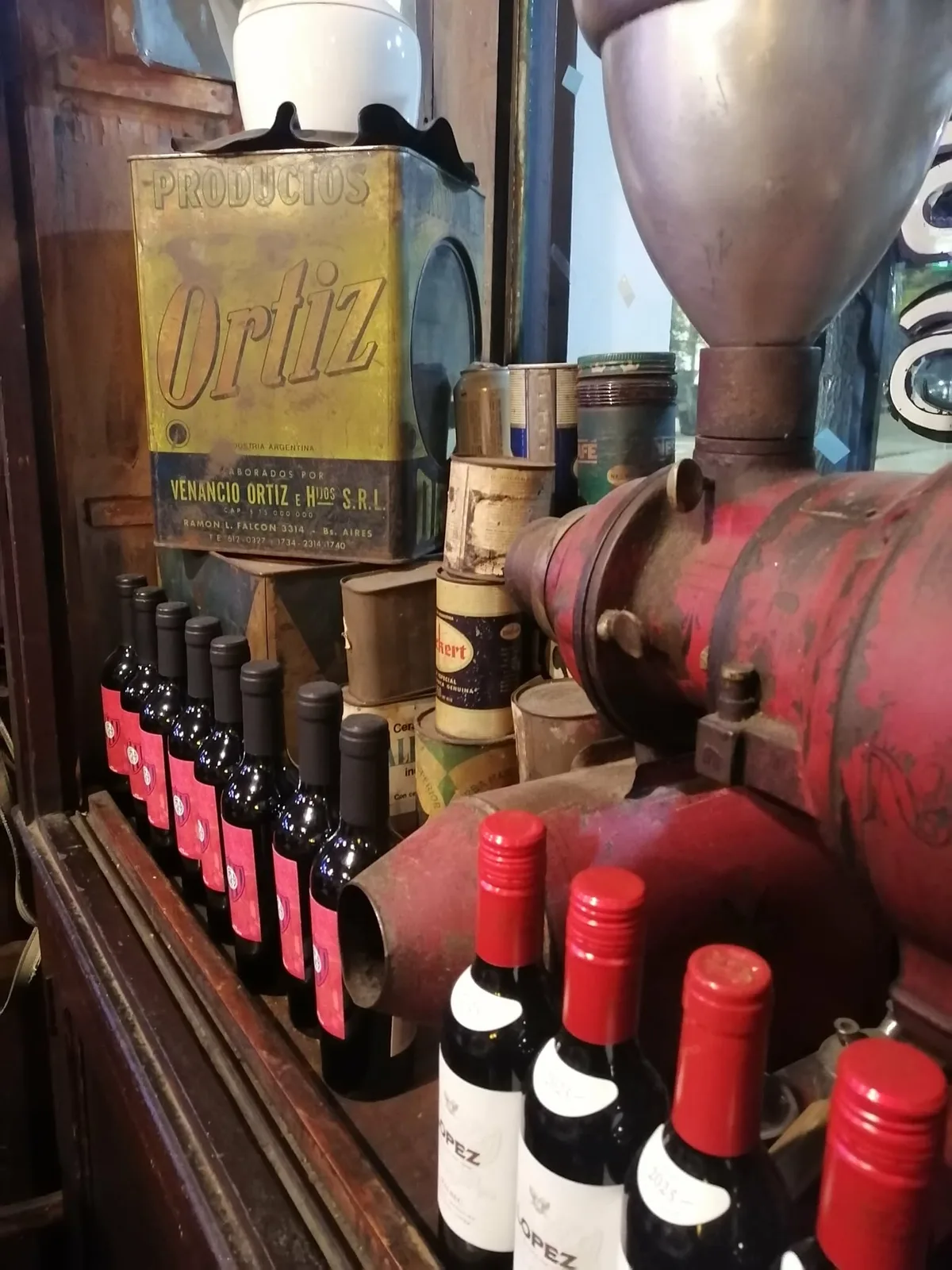 古い店の棚。色あせた「Ortiz」の大きなブリキ缶や古い缶詰の横に、赤く塗られた業務用のコーヒーミルが置かれている