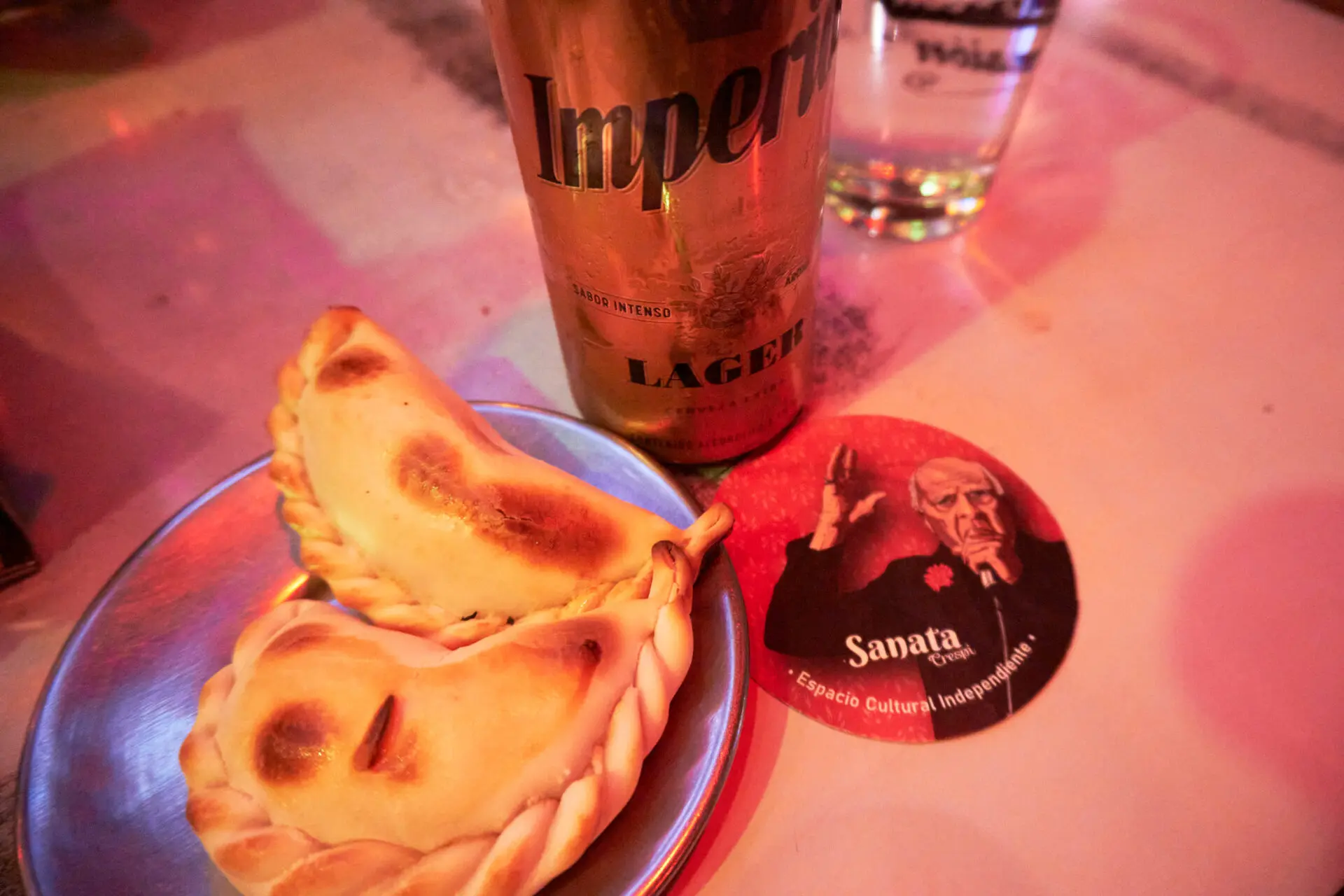 皿に載ったエンパナーダ2つとビール、サナタバーのコースター