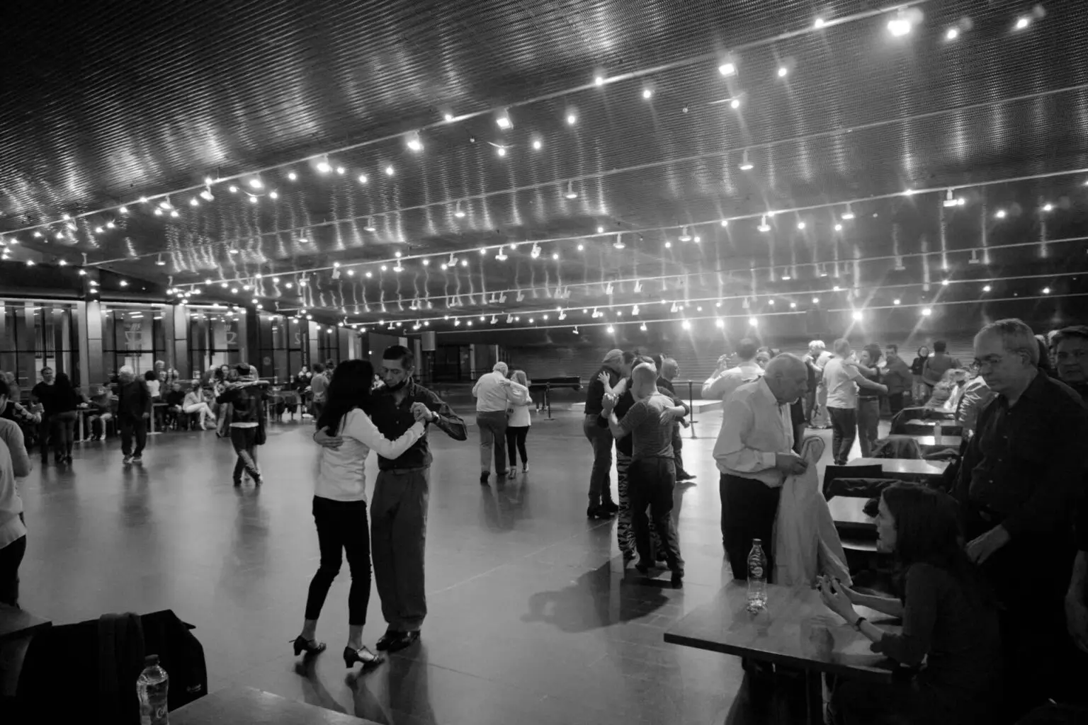 ミロンガ会場の全景。フロアの奥で数組が踊り、手前にはテーブルと椅子が並んでいる