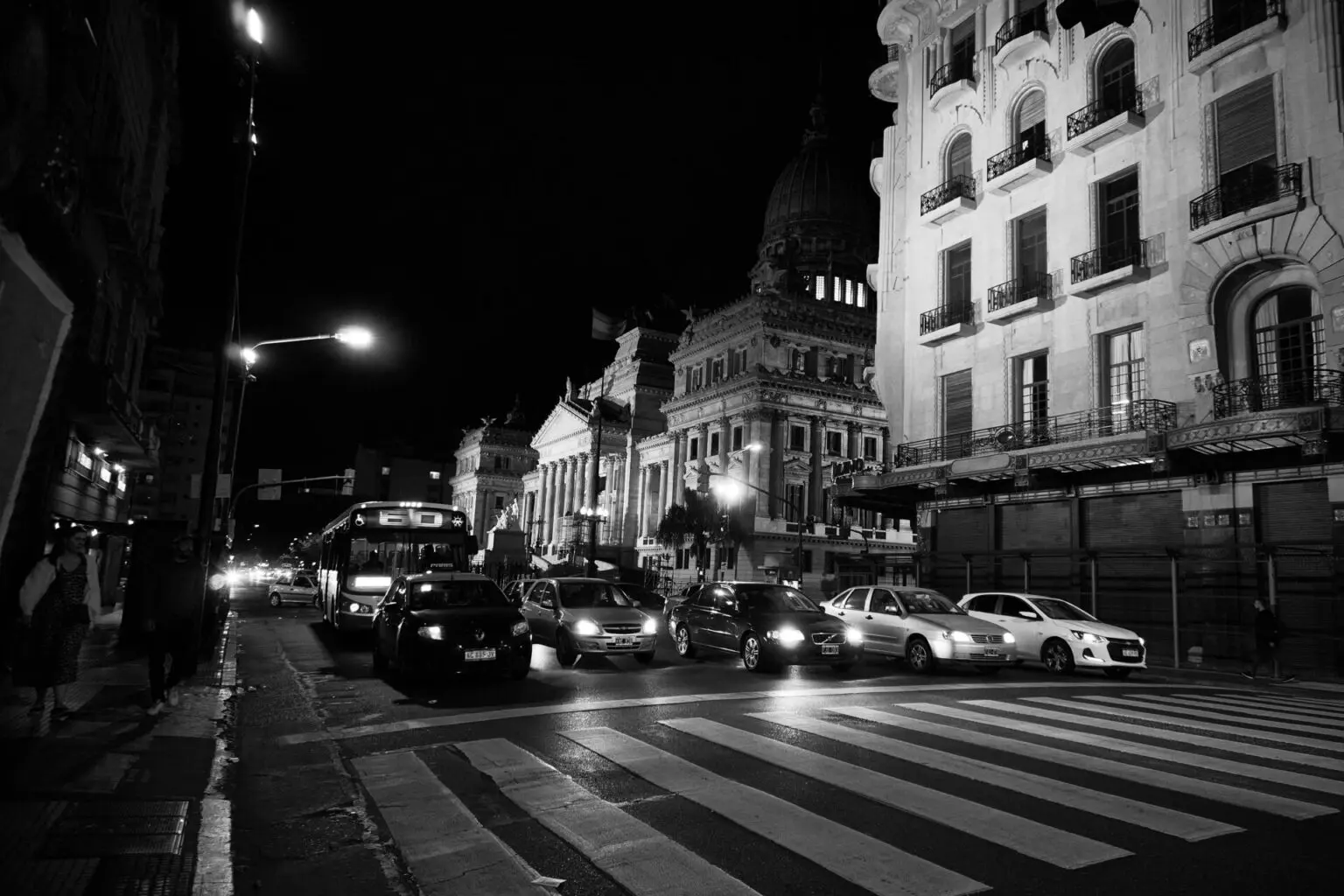 夜の国会議事堂前。ライトアップされた建物の手前に、バスと乗用車が信号待ちで並んでいる