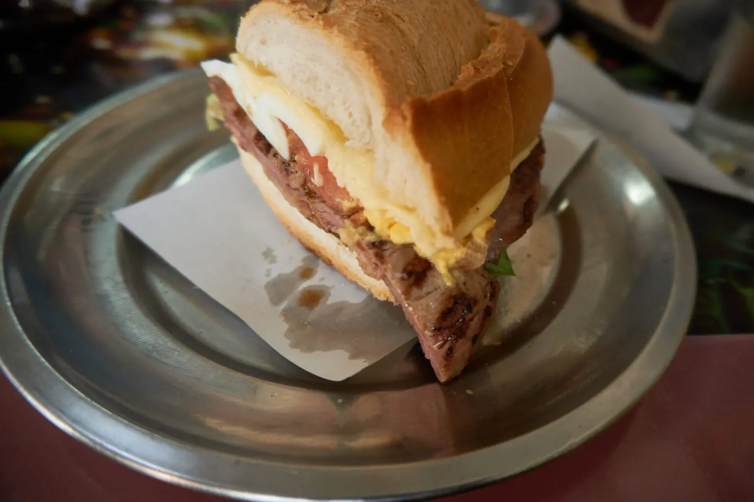 金属の皿に載ったロモのサンドイッチ。牛肉、ハム、チーズ、目玉焼きが挟まれている